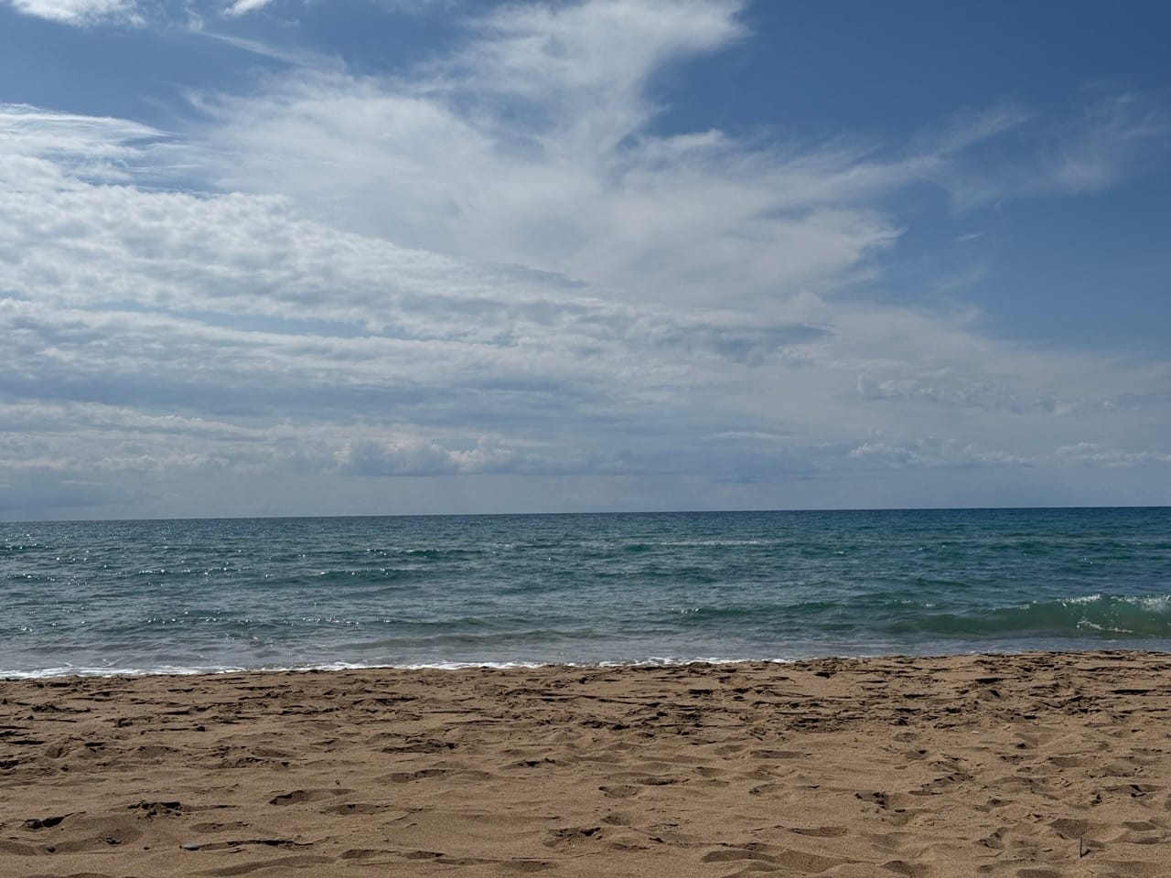 Vorne Strand, hinten leicht welliges Meer.