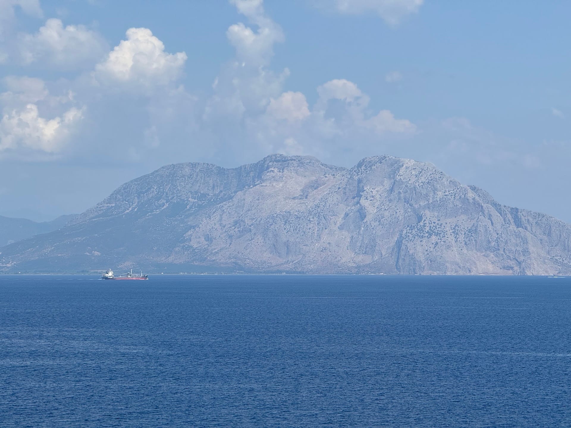 Vorne Meer, dahinter ein Tankschiff vor einem Berg.