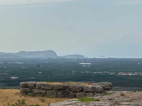 Im Vordergrund eine Ruine, im Hintergrund eine Ebene, ganz hinten Nafplio und das Meer.