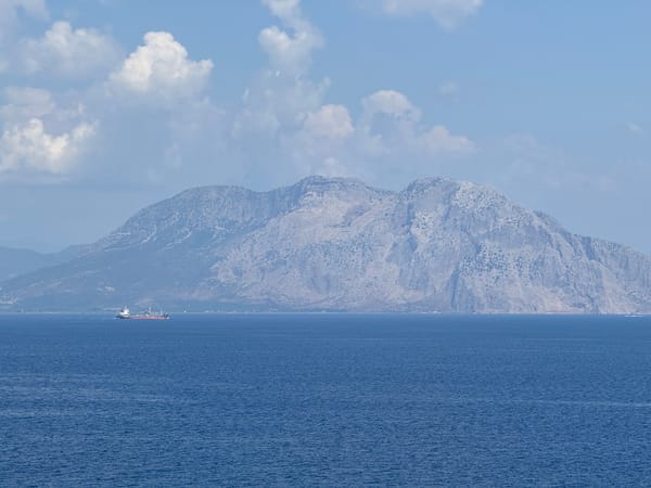 Vorne Meer, dahinter ein Tankschiff vor einem Berg.